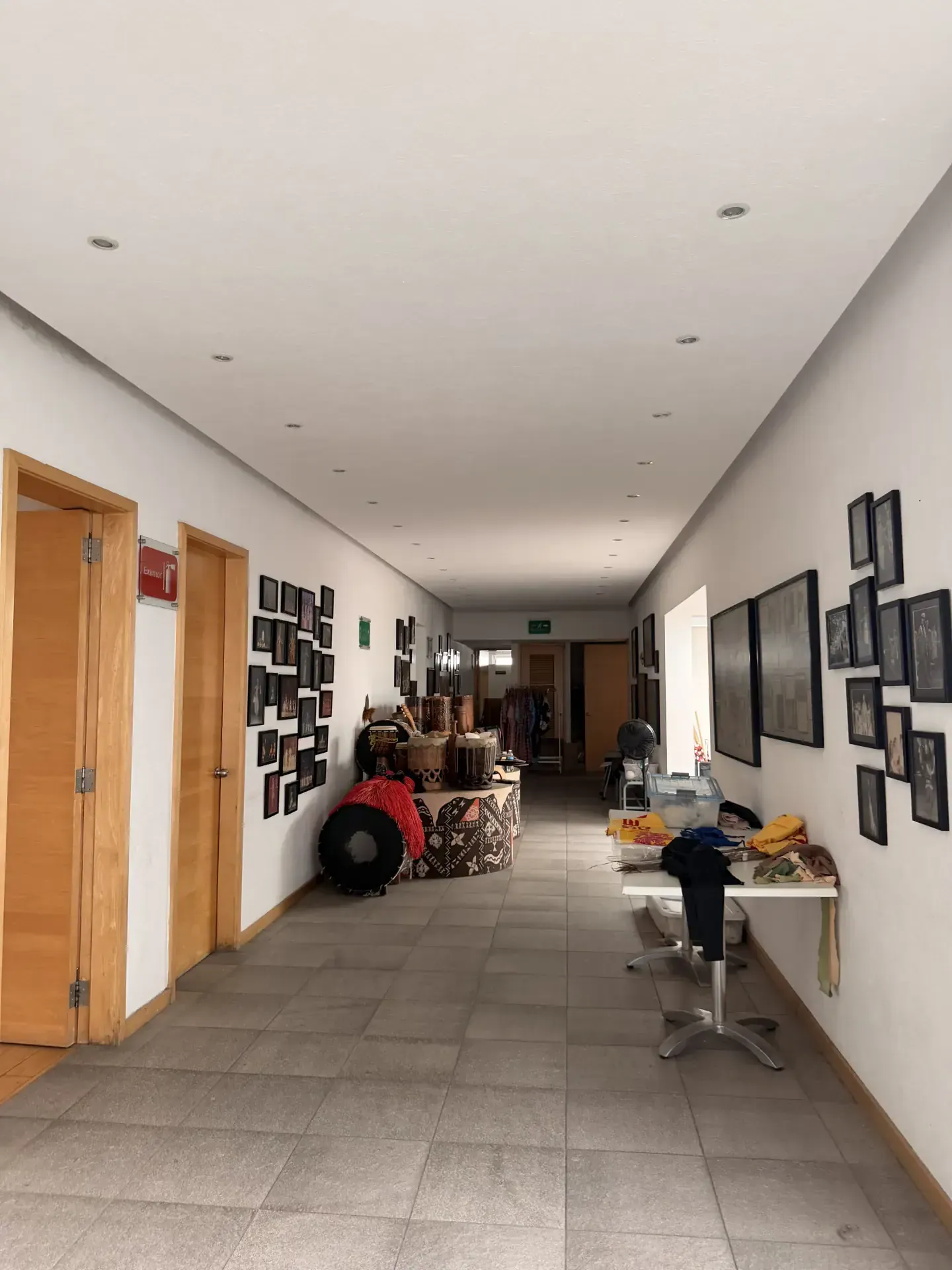 Pasillo largo y luminoso con paredes blancas, puertas de madera, cuadros y objetos decorativos en exhibición.